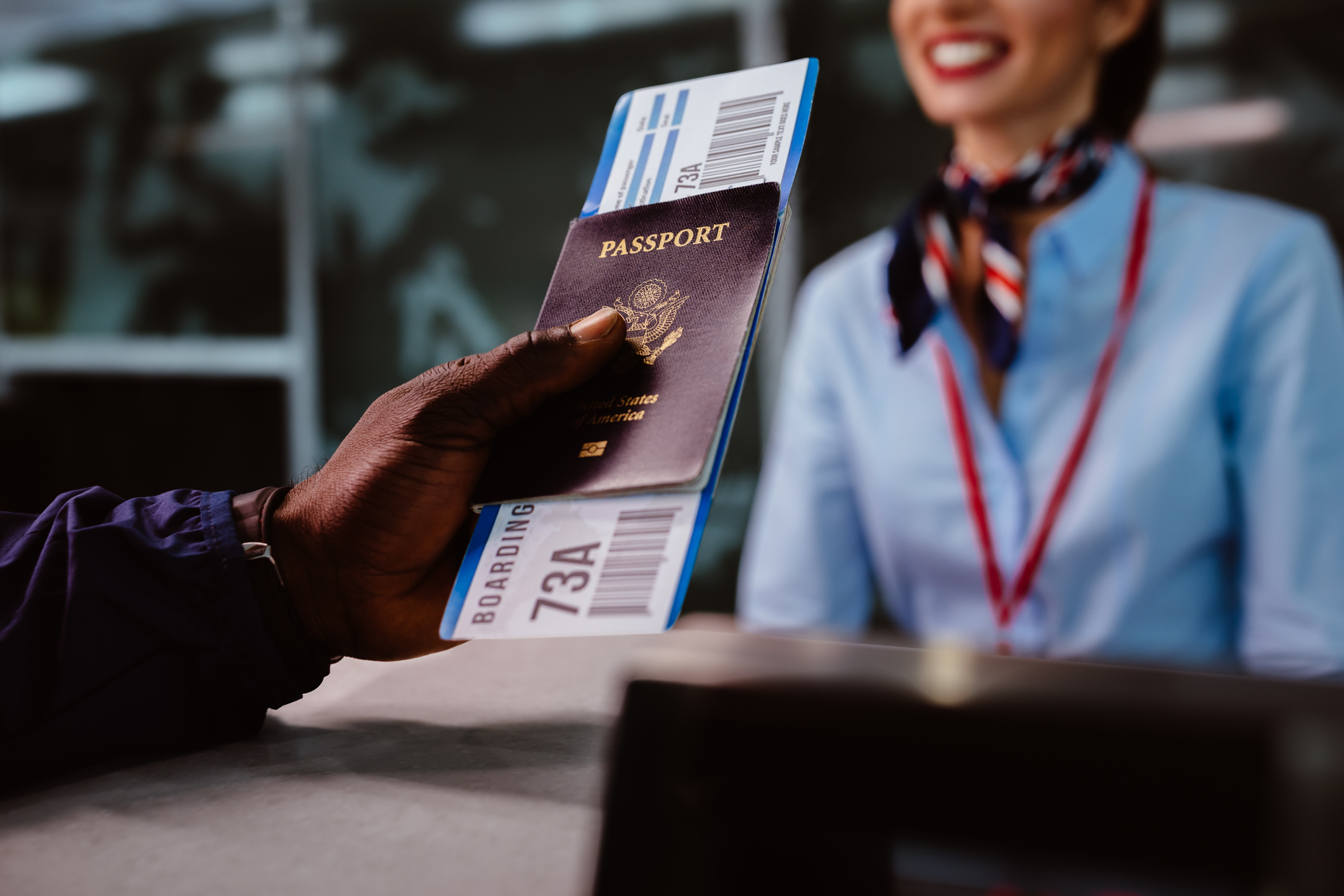 close-up van een mannenhand met een paspoort en een vliegticket reikend naar een stewardess aan een loket