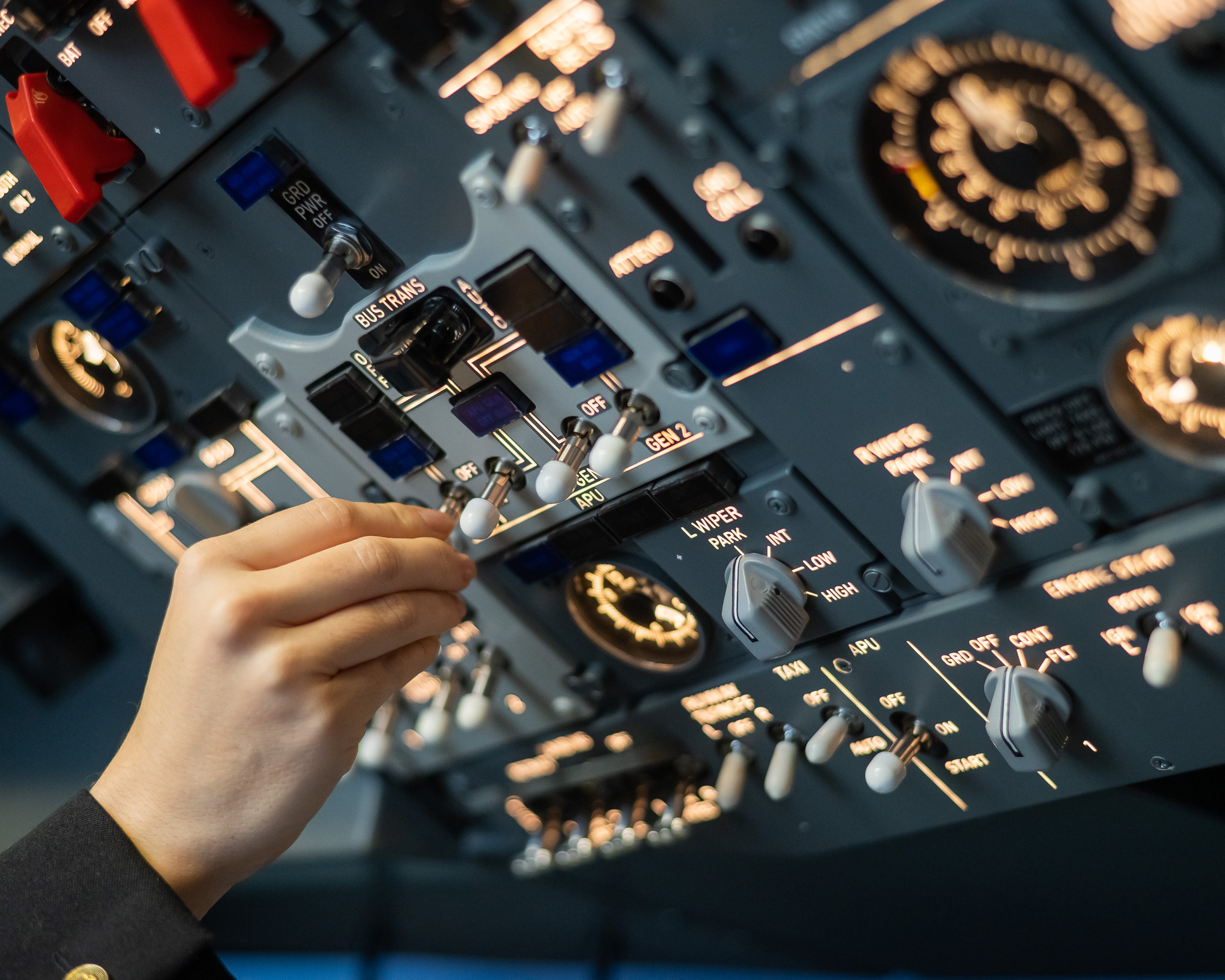 Een hand bedient een kleine schakelaar op een groot bedieningspaneel met talloze meters en hendels in de cockpit.