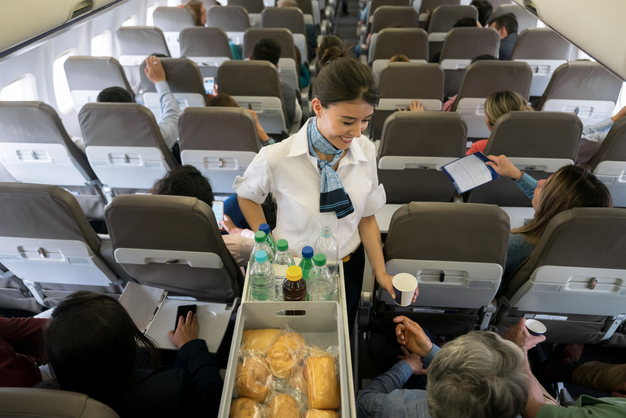 Een lachende stewardess overhandigt een drankje aan een passagier.
