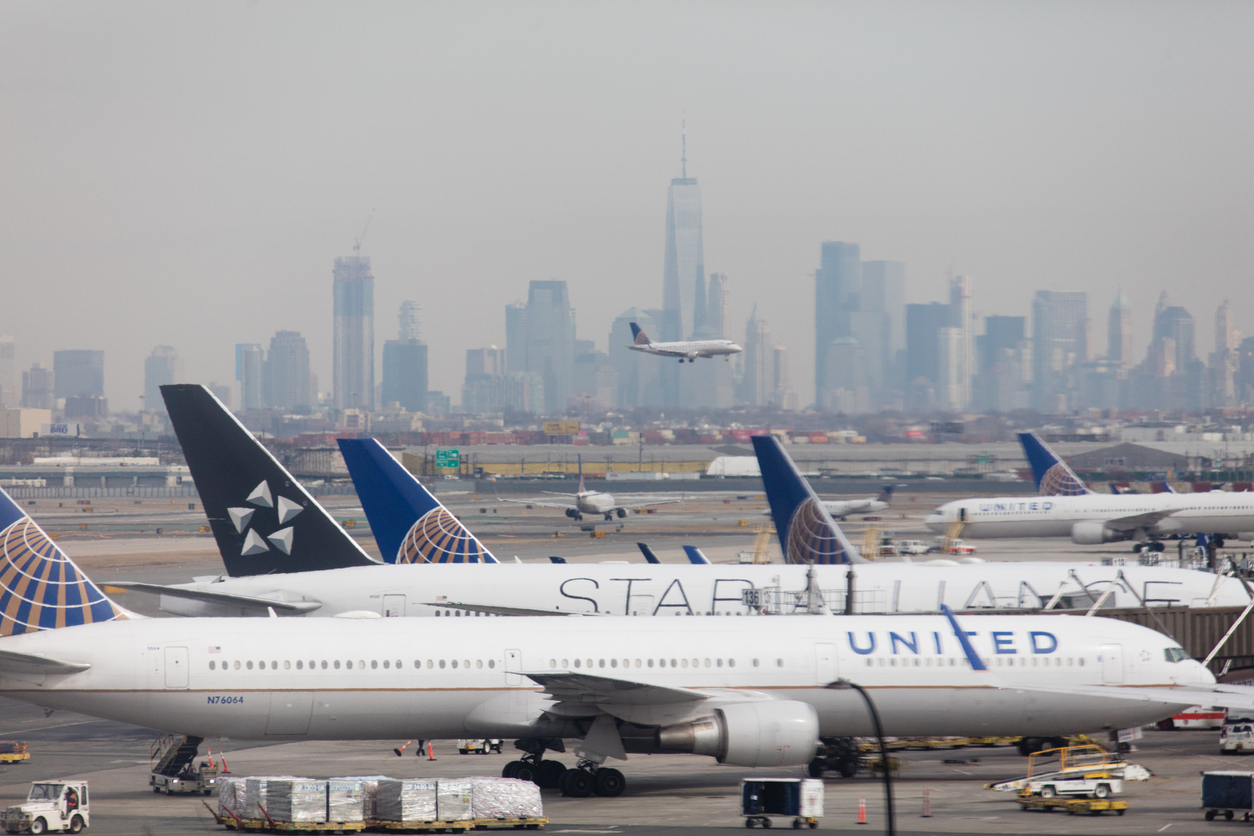 Een tarmac met een vliegtuig dat landt en de skyline van Manhattan op de achtergrond.