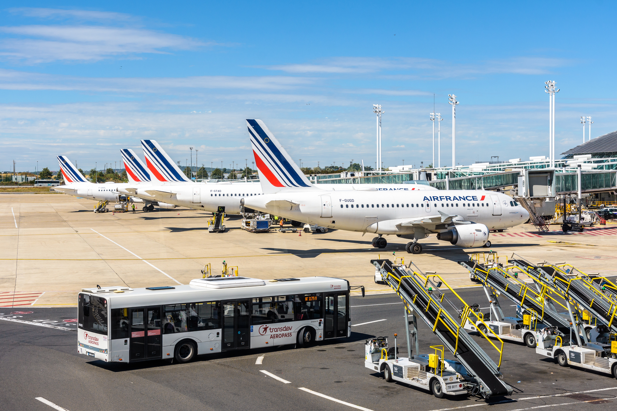 Een rij Air France vliegtuigen staat naast elkaar geparkeerd, op de voorgrond brengt een bus passagiers naar de vliegtuigen.