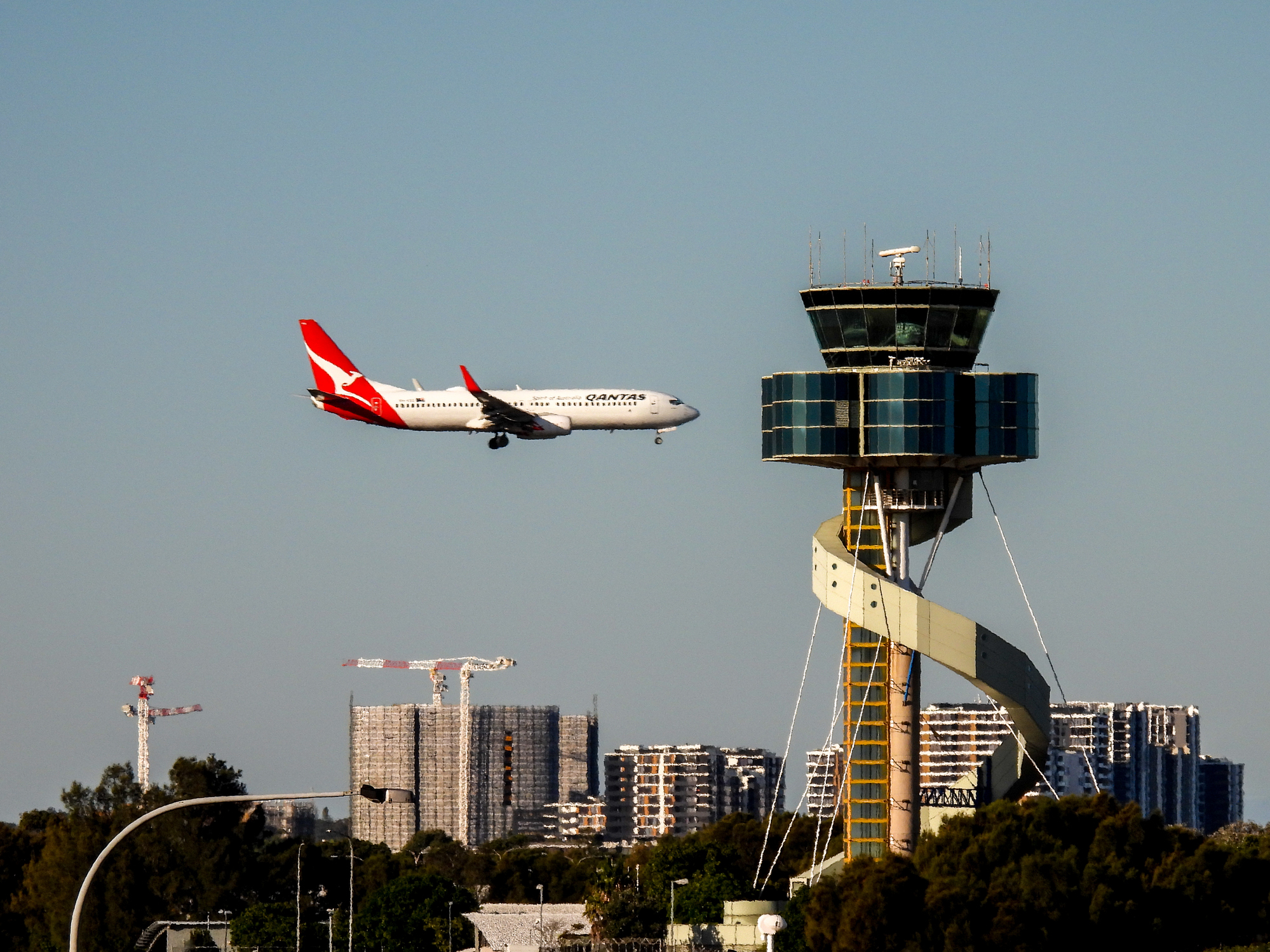 Een Qantas-vliegtuig nadert Sydney Airport, met de kenmerkende luchthaventoren verder naar achteren.