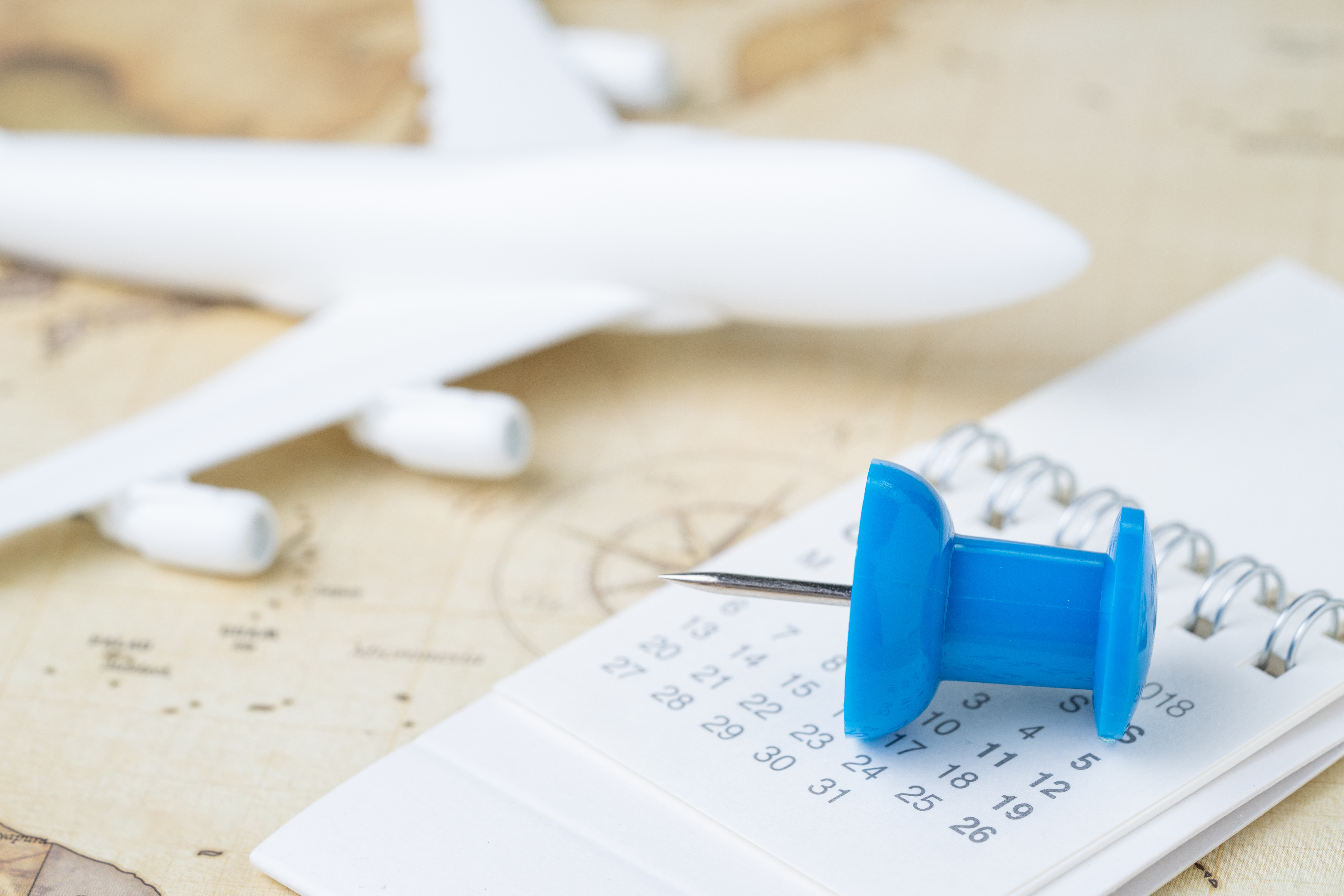 Open kalender met een blauwe speld in focus met een wazig modelvliegtuig op een kaart op de achtergrond