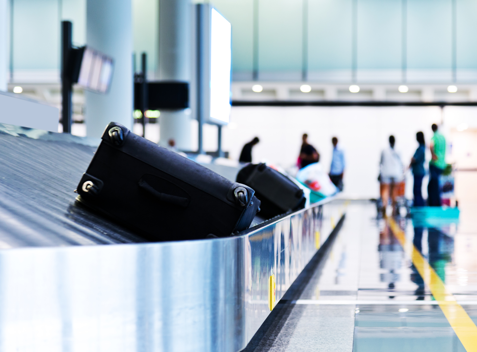 Bagageband op vliegveld met twee zwarte koffers op de voorgrond en een aantal wachtende mensen op de achtergrond