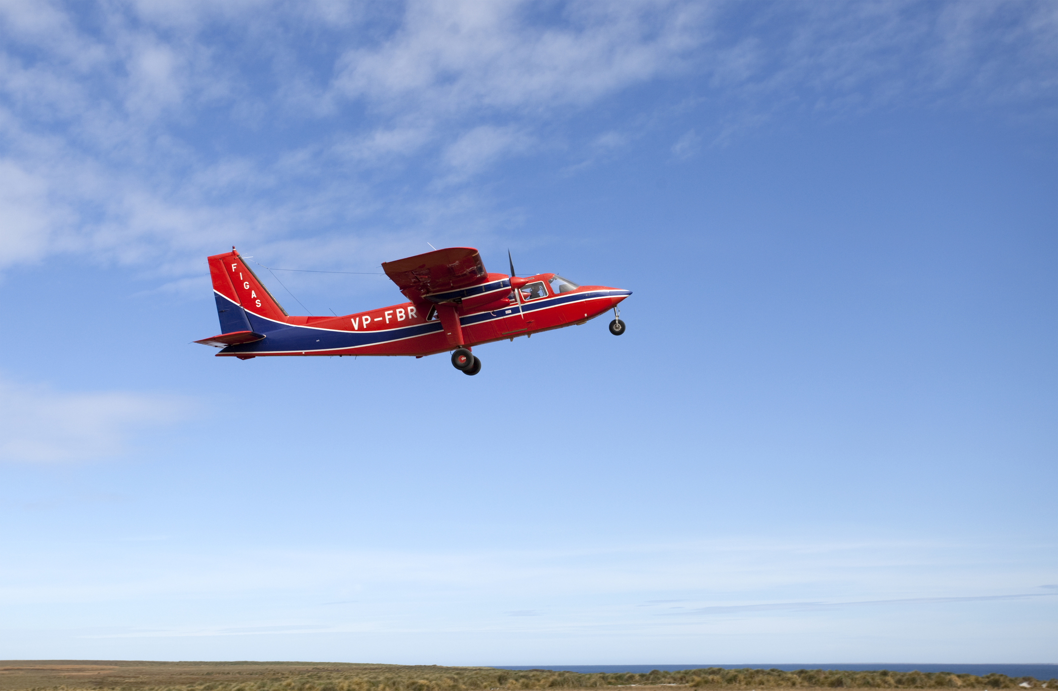 Een rood-blauw propellervliegtuig stijgt op bij mooi weer.