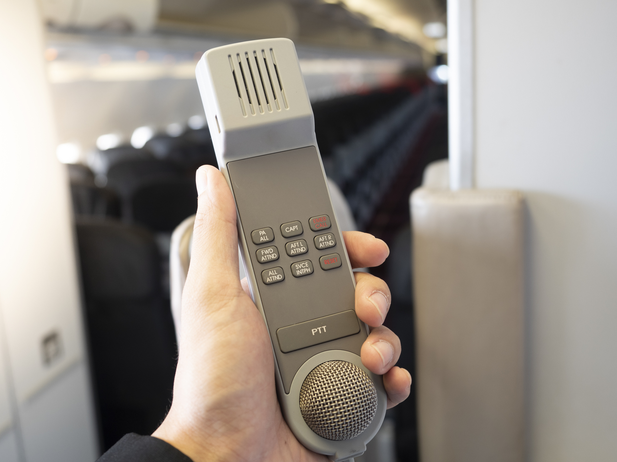 Mannelijk cabinepersoneel met een intercom in zijn hand in de cabine van een vliegtuig.