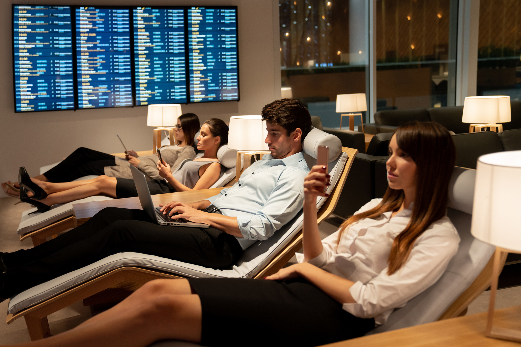 Slim geklede zakenreizigers ontspannen in een VIP-lounge op een luchthaven, op hun mobiele telefoon of laptop tijdens het wachten op hun vlucht
