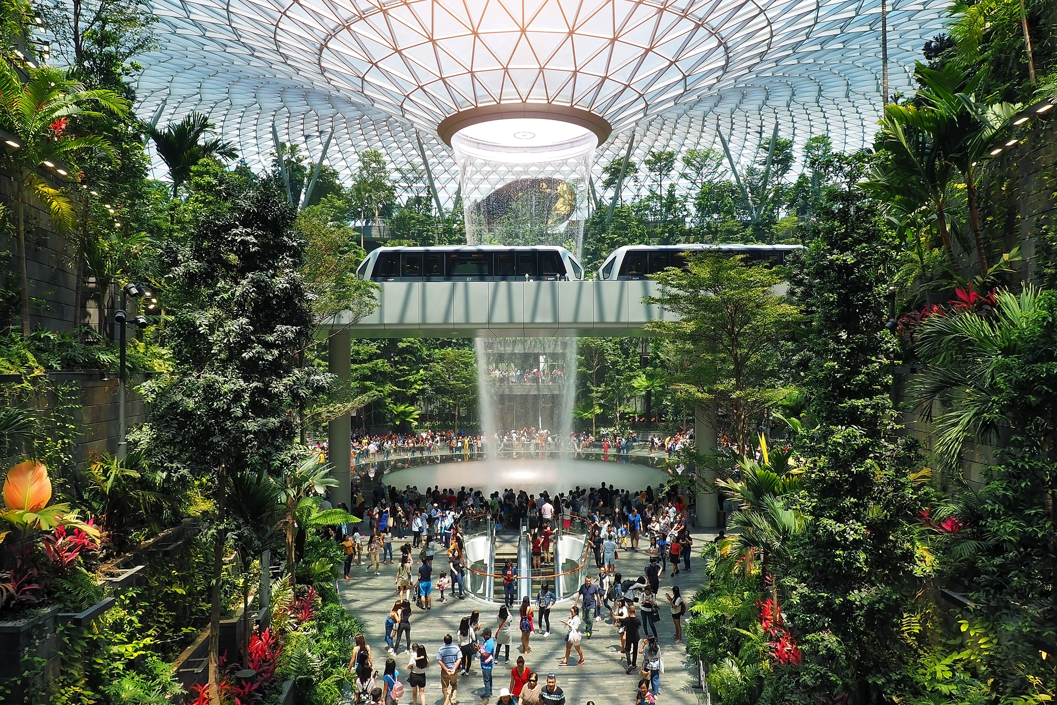 Een panoramafoto van binnenin het Jewel Changi, met de Rain Vortex waterval, tropische planten en vele reizigers.