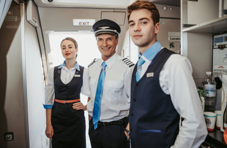 De piloot en twee stewardessen begroeten lachend passagiers.