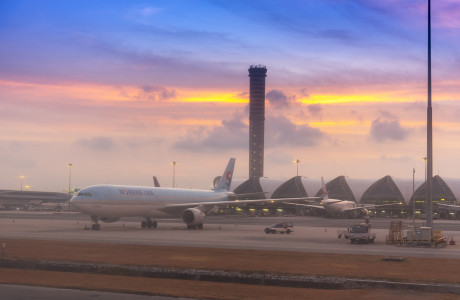 Een vliegtuig van Korean Air staat in de schemering op de tarmac op de voorgrond, terwijl de luchthaventoren van Bangkok Suvarnabhumi Airport op de achtergrond het luchtruim kiest.