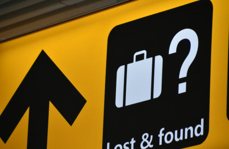Richtingaanwijzers op een geel bord op een luchthaven met witte letters "Lost & Found" en een koffer afgebeeld in het wit op een zwarte achtergrond