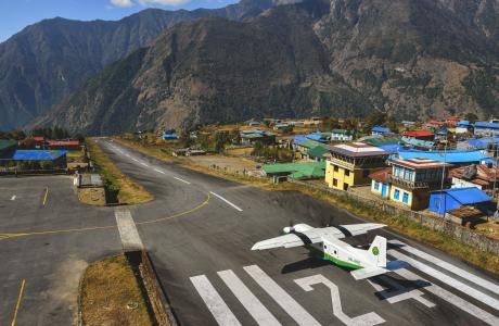 De startbaan in Lukla bij goed weer, een propellervliegtuig begint zojuist met opstijgen.
