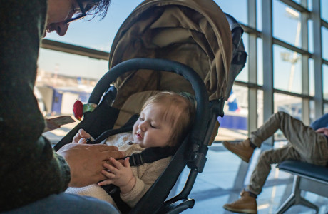 Een man zit in een luchthaventerminal en speelt met een baby in een kinderwagen.