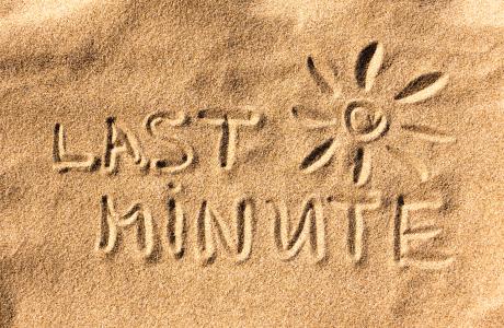 De woorden “Last Minute” en een zon zijn in het zand getekend.