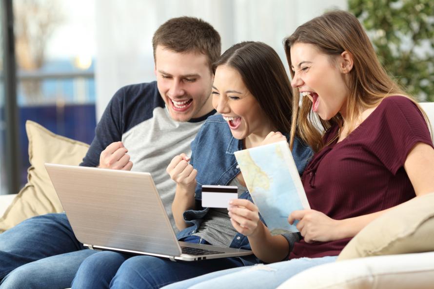 Drie jonge mensen zitten juichend voor een laptop.